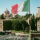 Italian flag waving over Rome cityscape with historic buildings and pedestrians in summer.