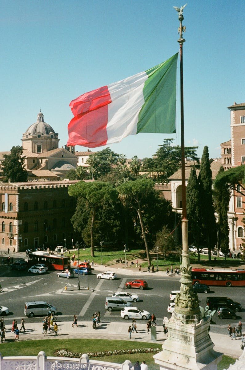 Italian flag waving over Rome cityscape with historic buildings and pedestrians in summer.
