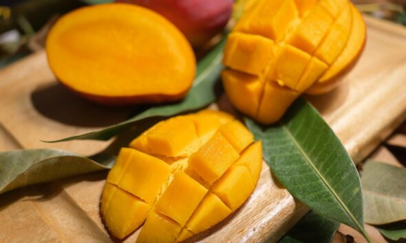Close-up of ripe mango slices on a wooden board with leaves. Perfect for tropical fruit themes.