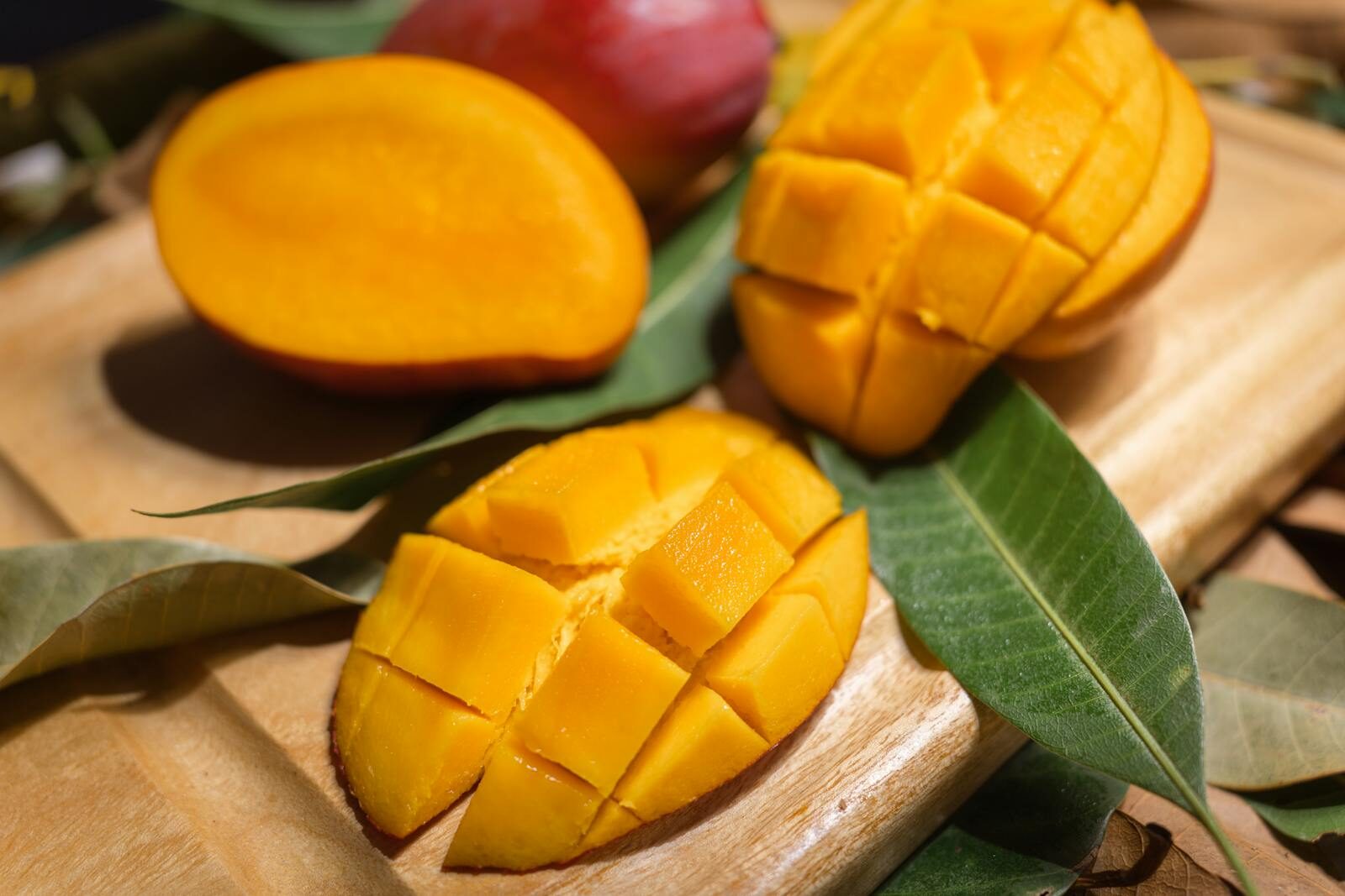 Close-up of ripe mango slices on a wooden board with leaves. Perfect for tropical fruit themes.