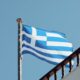 The Greek flag waves on a clear day in Naxos, Greece, showcasing Aegean architecture.