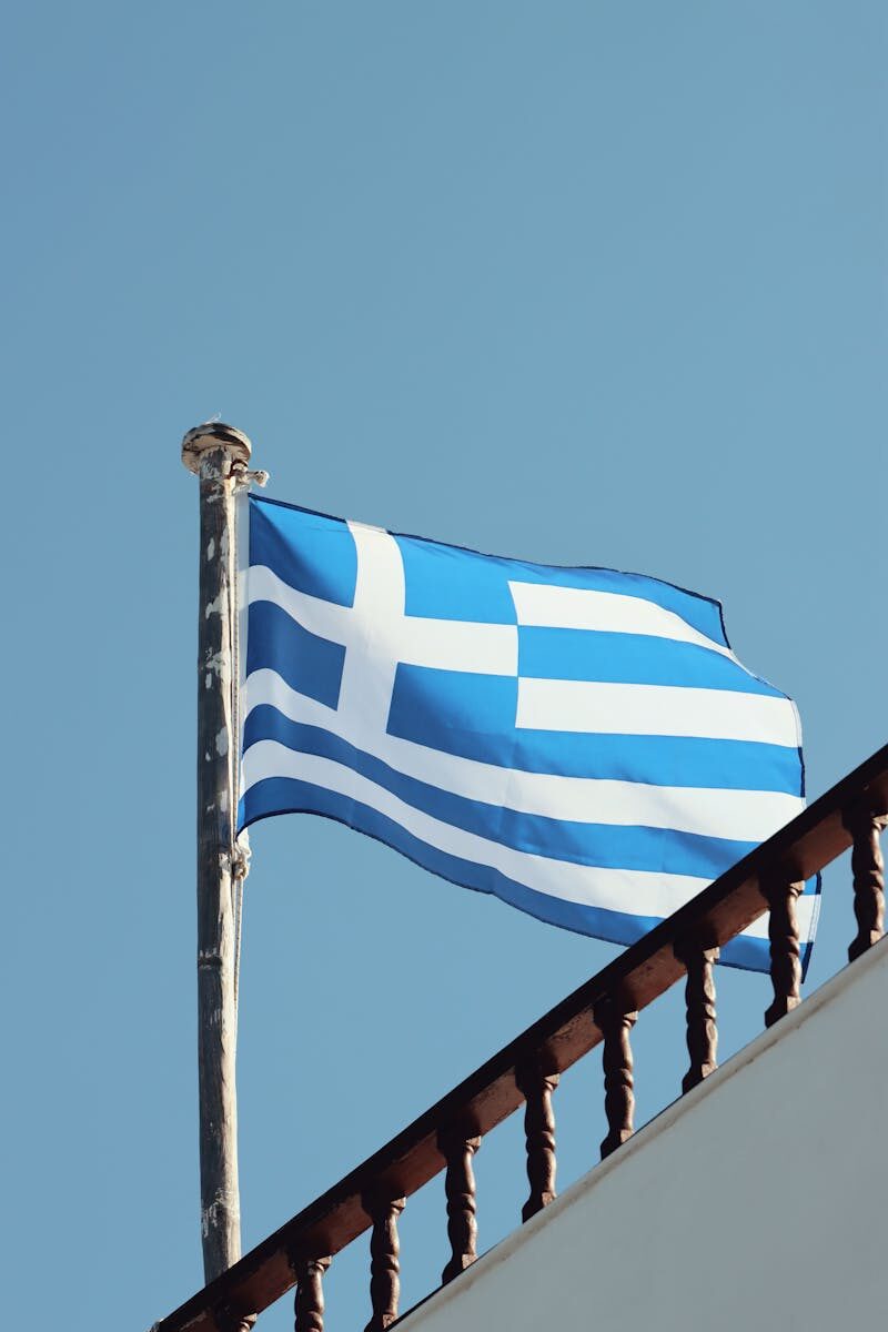 The Greek flag waves on a clear day in Naxos, Greece, showcasing Aegean architecture.