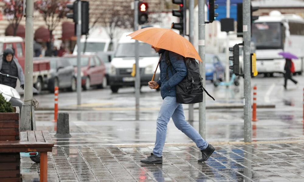 A man walks with an orange umbrella on a rainy day in Istanbul, Türkiye.