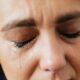 Closeup of crop unrecognizable middle aged woman suffering from depression and crying with closed eyes