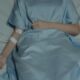 A patient lies in bed wearing a hospital gown with an IV drip attached, evoking a sense of illness.