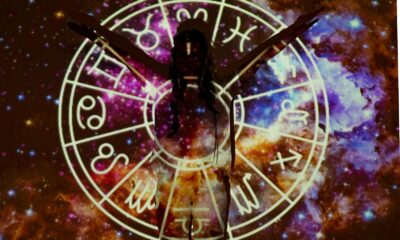 Silhouette of person extending arms against zodiac symbols and cosmic background, esoteric theme.