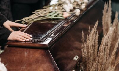 Mourners at a funeral with floral arrangements on a polished wooden coffin.