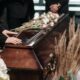 Mourners at a funeral with floral arrangements on a polished wooden coffin.