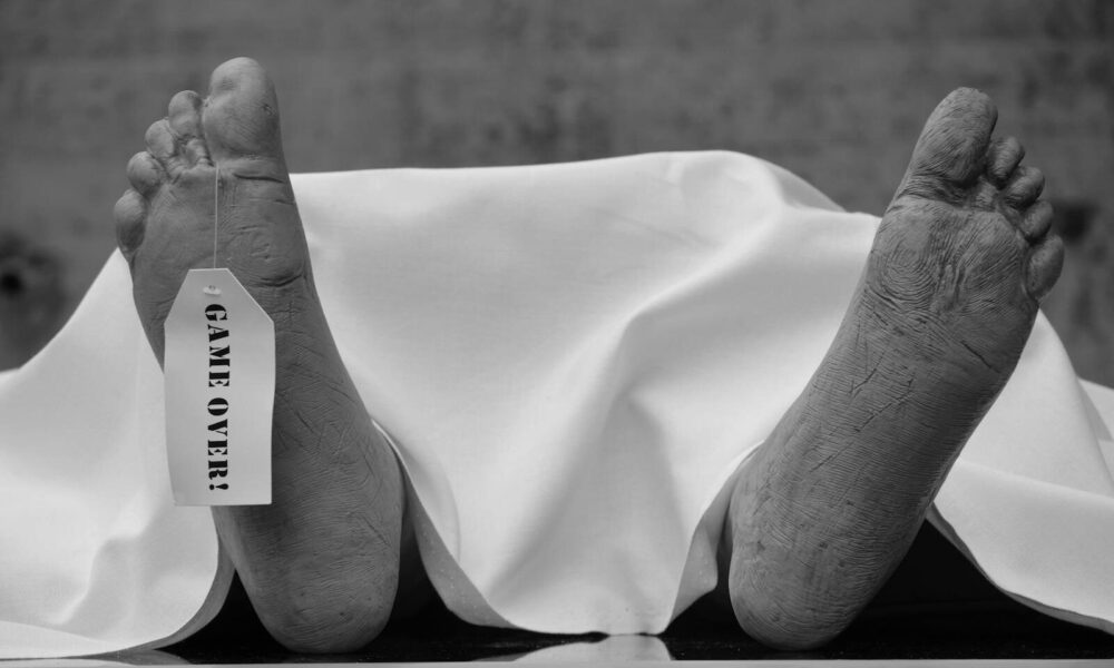Conceptual black and white photo with symbolic 'Game Over' tag on feet.