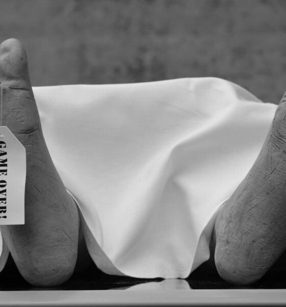 Conceptual black and white photo with symbolic 'Game Over' tag on feet.