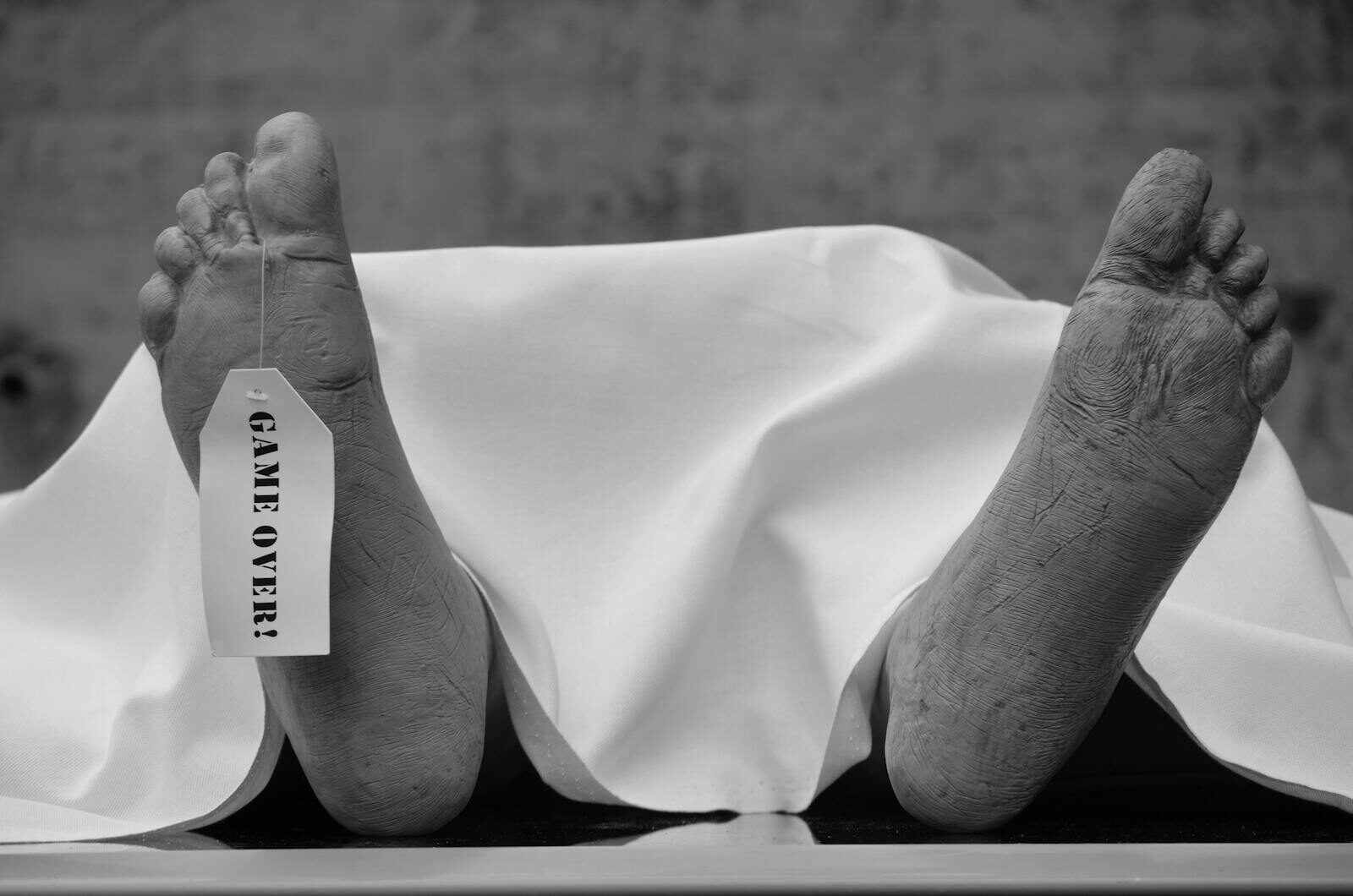 Conceptual black and white photo with symbolic 'Game Over' tag on feet.
