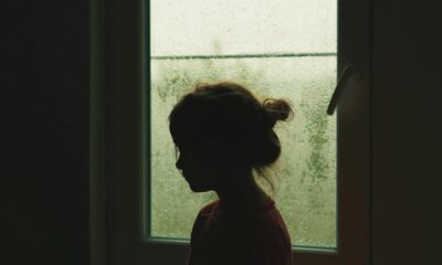 A child's silhouette stands by a rainy window, creating a nostalgic indoor scene.