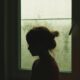 A child's silhouette stands by a rainy window, creating a nostalgic indoor scene.