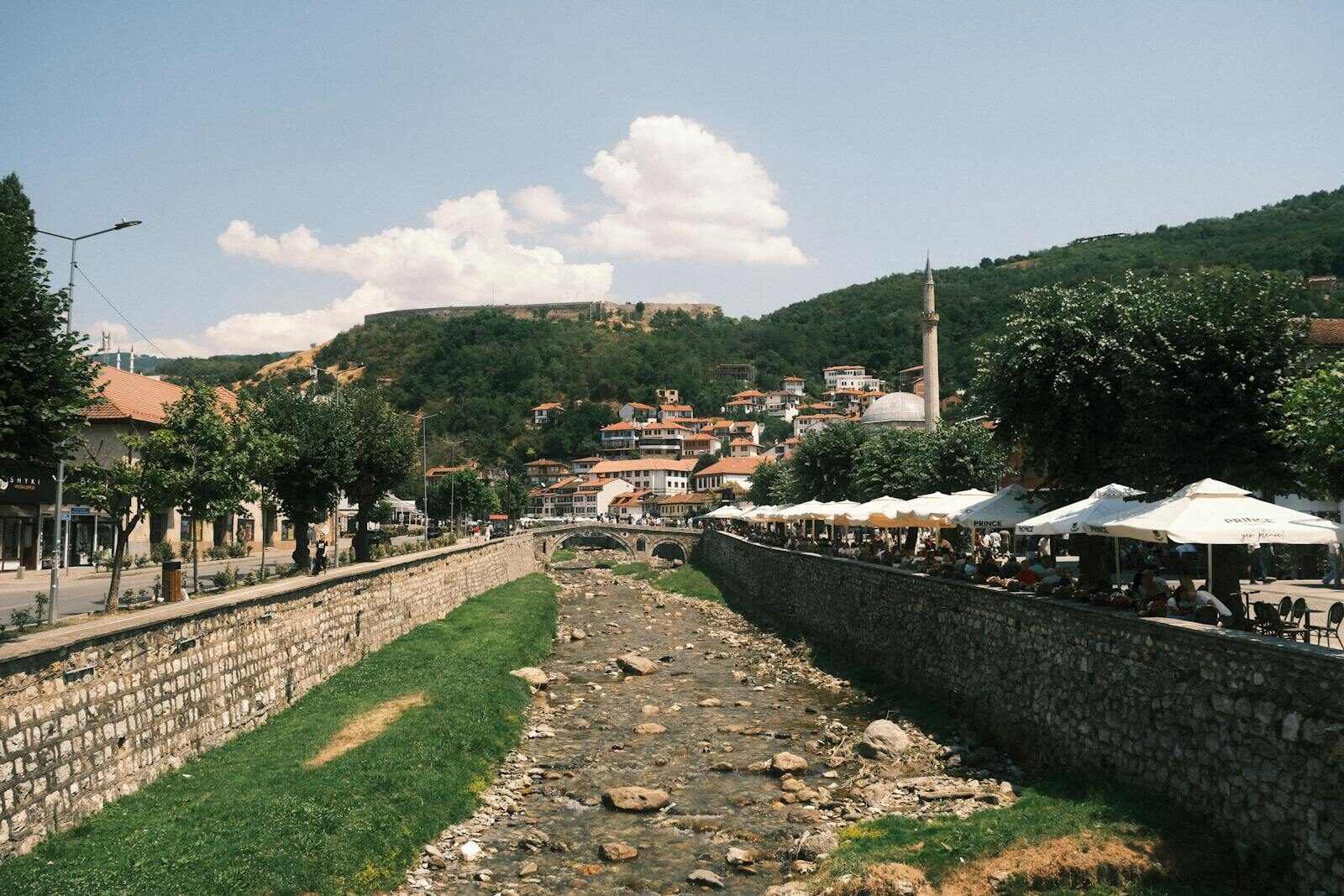 Panoramic view of Prizren's charming riverside cafes and historic architecture on a sunny day.