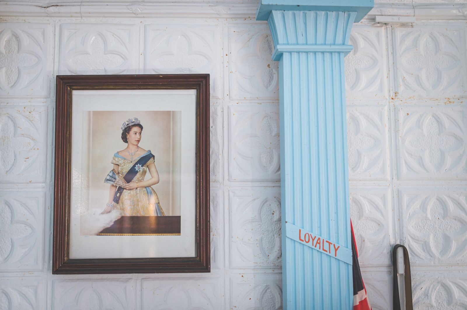 Framed portrait of a queen beside a blue column with loyalty sign.