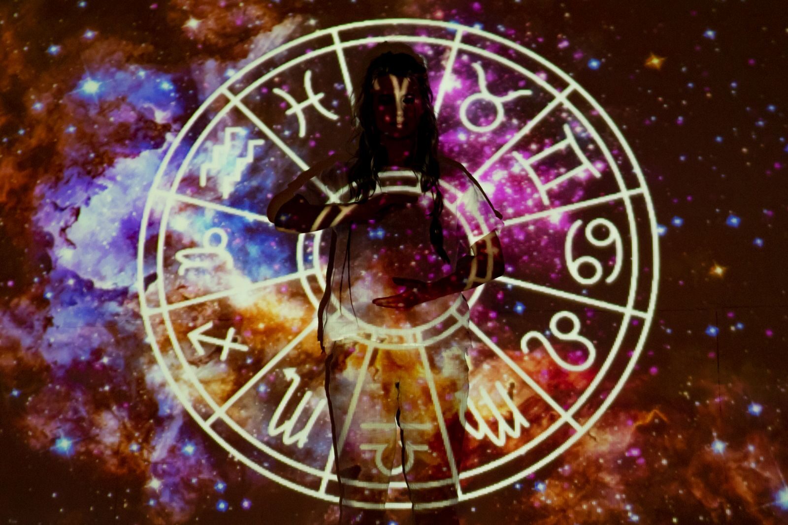 Woman standing with astrological symbols projected, evoking a mystical vibe.