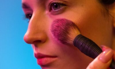 Close-up of a woman applying makeup with a brush against a vibrant backdrop.