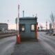 Industrial checkpoint and barrier at port under cloudy sky with cranes in the background.