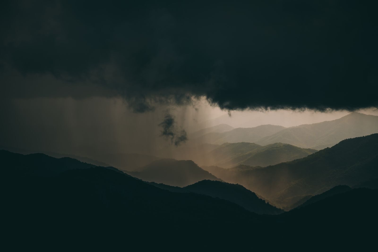 A breathtaking view of mountainous hills beneath dramatic storm clouds at sunset.