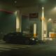 A BMW sports car parked at a Shell gas station at night, featuring bright lights and an urban setting.