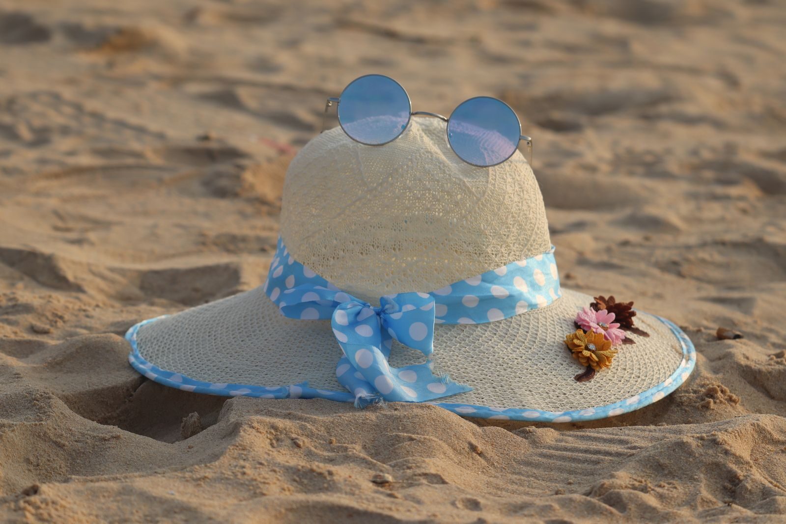 Charming straw hat adorned with flowers and sunglasses on a sunny beach day.