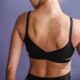 Back view of crop anonymous female in black sportive underwear standing against purple background in studio