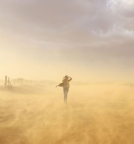 A woman braves a windy desert in Utah, creating a picturesque scene with dust and soft light.