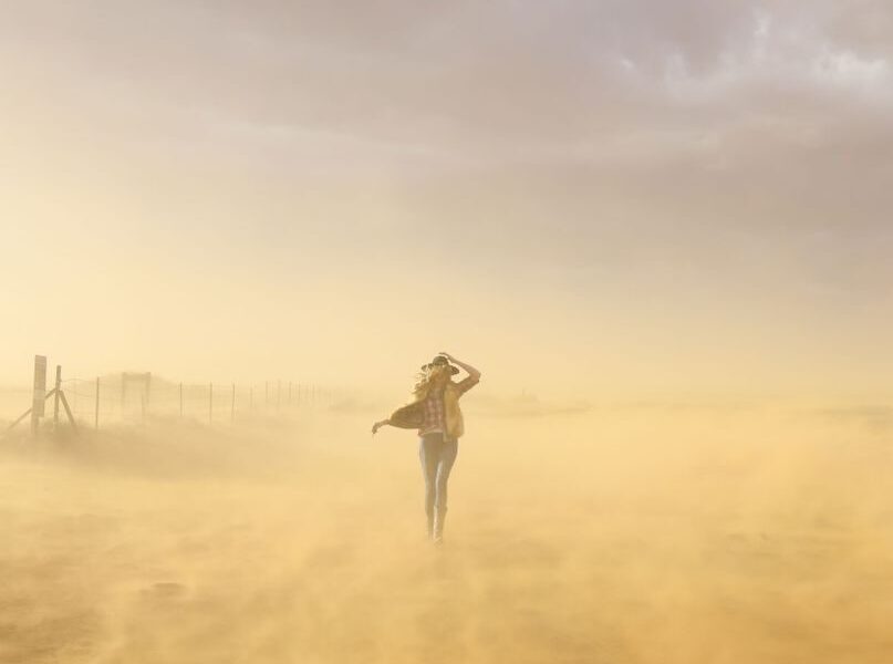 A woman braves a windy desert in Utah, creating a picturesque scene with dust and soft light.