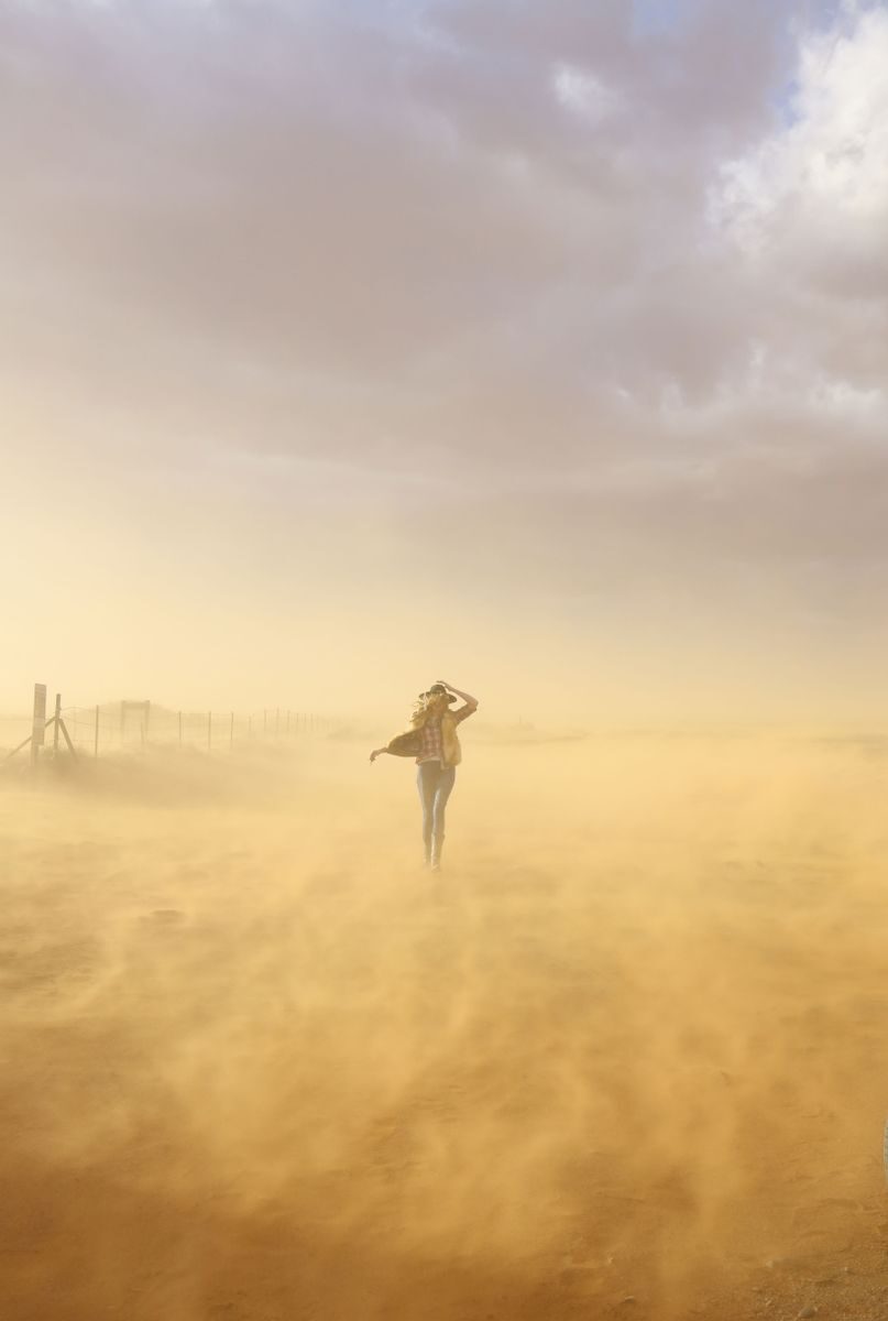 A woman braves a windy desert in Utah, creating a picturesque scene with dust and soft light.