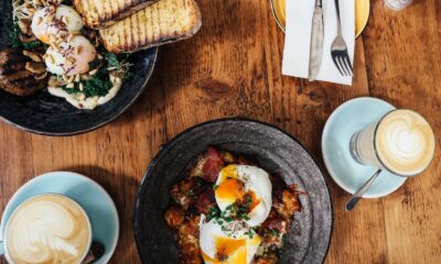 Top view of a delightful brunch spread featuring poached eggs and lattes on a wooden table.