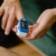 Hands of an adult using a pulse oximeter device to measure oxygen levels indoors.