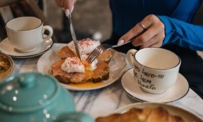 Woman enjoying breakfast with poached eggs, toast, and tea in a cozy setting.