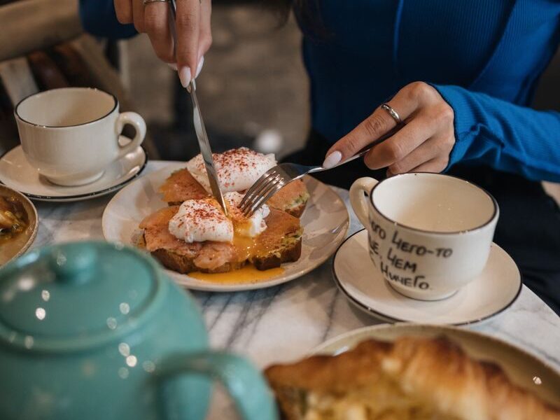 Woman enjoying breakfast with poached eggs, toast, and tea in a cozy setting.