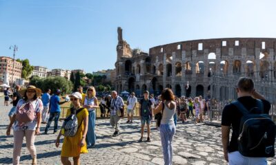 Tourists wander around the iconic Colosseum in Rome on a clear summer day, capturing memories.