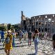 Tourists wander around the iconic Colosseum in Rome on a clear summer day, capturing memories.