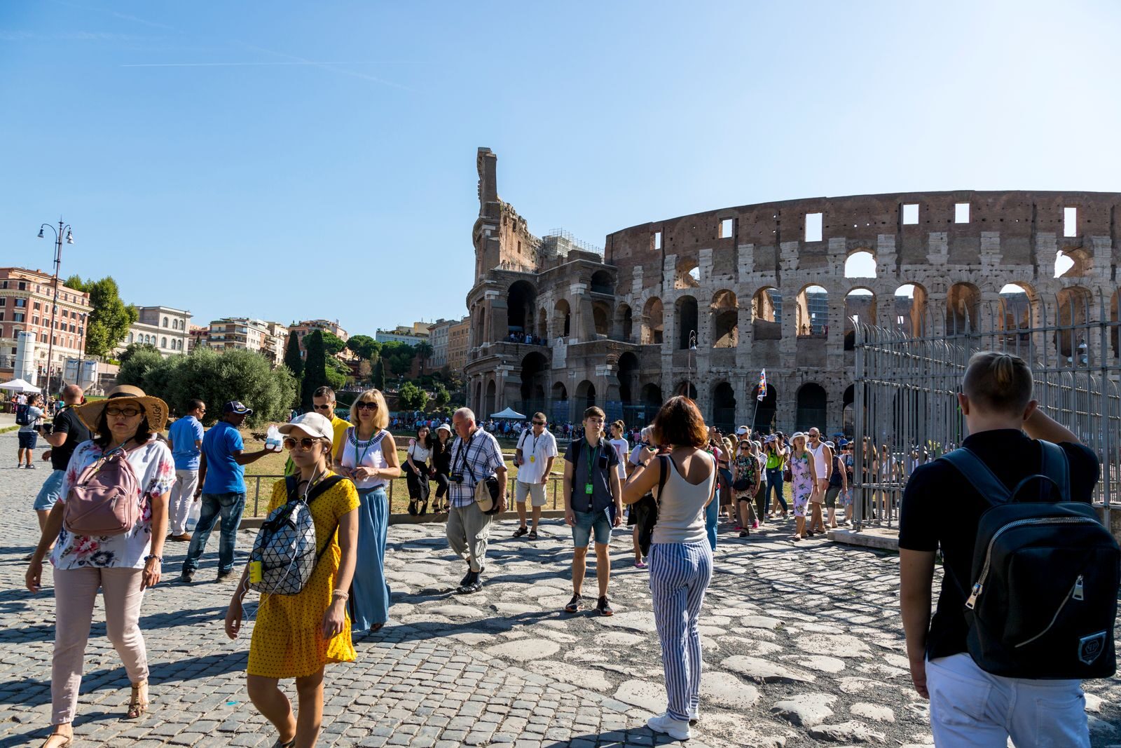 Tourists wander around the iconic Colosseum in Rome on a clear summer day, capturing memories.