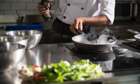 Chef prepares food in a sleek kitchen using a frying pan on an induction cooktop.