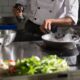 Chef prepares food in a sleek kitchen using a frying pan on an induction cooktop.