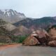 A scenic mountain road blocked by large rocks from a landslide with a snowy peak in the background.