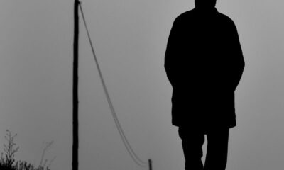 Silhouette of a man with hat walking on a rural path, black and white style.