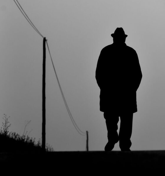 Silhouette of a man with hat walking on a rural path, black and white style.