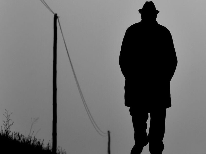 Silhouette of a man with hat walking on a rural path, black and white style.