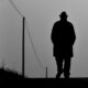 Silhouette of a man with hat walking on a rural path, black and white style.