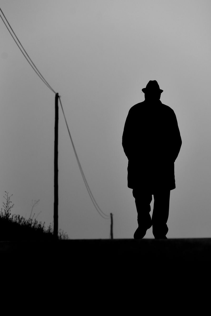Silhouette of a man with hat walking on a rural path, black and white style.