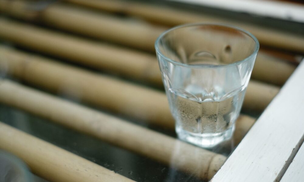 A shot glass with clear liquid placed on a bamboo surface, creating a reflective and calming scene.