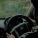 Close-up of a man driving a car, focusing on the steering wheel and interior setup.