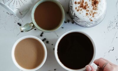 Top view of various coffee drinks and a hand selecting a cup in a cozy İstanbul cafe setting.