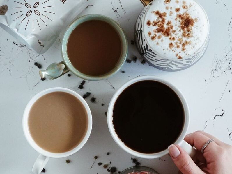 Top view of various coffee drinks and a hand selecting a cup in a cozy İstanbul cafe setting.