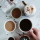 Top view of various coffee drinks and a hand selecting a cup in a cozy İstanbul cafe setting.