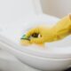 From above of crop anonymous person in rubber gloves using soapy sponge while cleaning toilet bowl